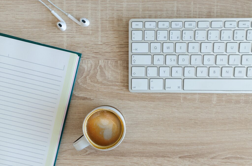 机の上にあるノートとキーボードとイヤホンとコーヒーカップ