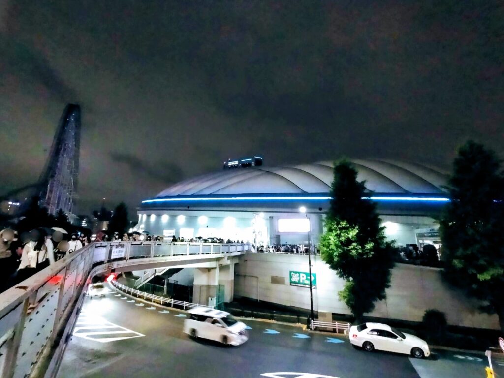 ライトアップされた夜の東京ドームと外を歩いている人々。